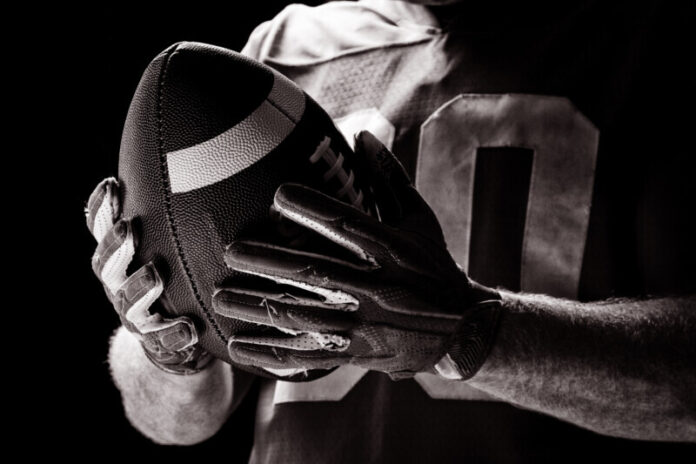 Mid section of American football player holding rugby ball