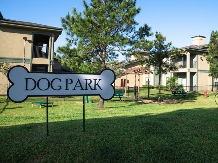 Community on-site dog park at the grassy backyard of a typical apartment complex building in suburban area at Humble, Texas, US. Off-leash dog park with pet stations, toys and bag dispensers Why dog park surfacing choices determine long-term success
